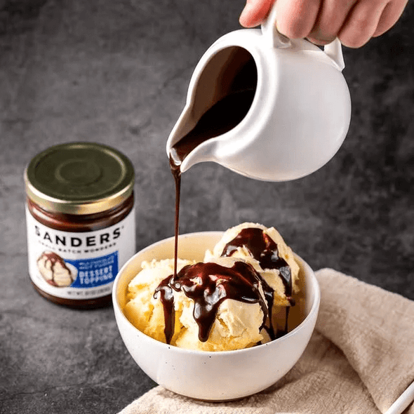 Pouring Milk Chocolate Hot Fudge Topping on vanilla ice cream in a bowl with Milk Chocolate Hot Fudge Topping at the back 